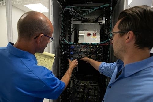 An image from behind the shoulders of two engineers reaching into a piece of equipment 